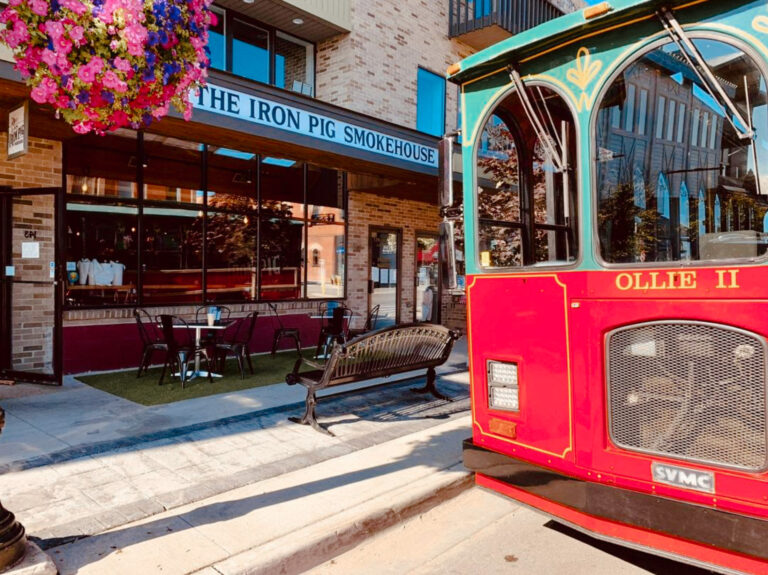 Outside view of Iron Pig Smokehouse as trolley passes. Sign reads “Iron Pig Smokehouse.”